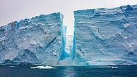 Ice crashing down from a massive iceberg into the deep blue ocean of Antarctica, forming a striking, jagged crack in the ice, AI generated [IBR125653458]