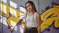 Portrait of a young woman with colorful braids and a tattoo standing in front of a graffiti wall, showcasing urban style and individuality, AI generated [IBR125653503]