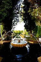 A round stone fountain with water fountains stands in the middle of a historic garden framed by tall cypress trees, Generalife, Alhambra, Granada, Granada province, Andalusia, Spain [IBR125657383]