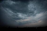 Dark storm clouds sweep across the sky above a nearly black distant landscape, with faint warm light near the horizon - Czech republic [IBR125657428]
