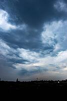 Heavy blue-gray storm clouds loom over a distant town silhouetted along the horizon - Czech republic [IBR125657437]