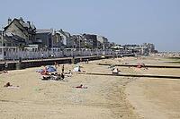 Luc-sur-Mer beach in Normandy, People relax on a wide sandy beach beneath a clear sky, with a seaside promenade and town buildings along the shore in France redactional use only [IBR125659389]