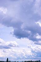 Fluffy white and gray clouds fill a pale blue sky above a distant tree-lined horizon [IBR125659405]