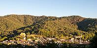 A panoramic view shows tiled village roofs, Saint-Pons ruins and a church tower beneath wooded hills in evening light in Collobrières, Var, Provence-Alpes-Cote d'Azur, France [IBR125659459]