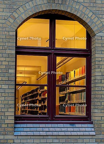A view through the window of a library, shelves full of books illuminated by a warm, yellow light, Berlin, Germany [IBR112672613]