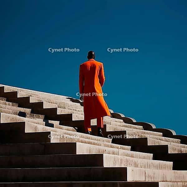 Dark-skinned man in orange coat standing on stairs with back, copy space, AI generated [IBR123435169]