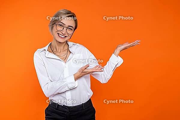 Beautiful blonde woman wearing white official style shirt pointing at copy space for advertisement isolated over orange background [IBR123569294]