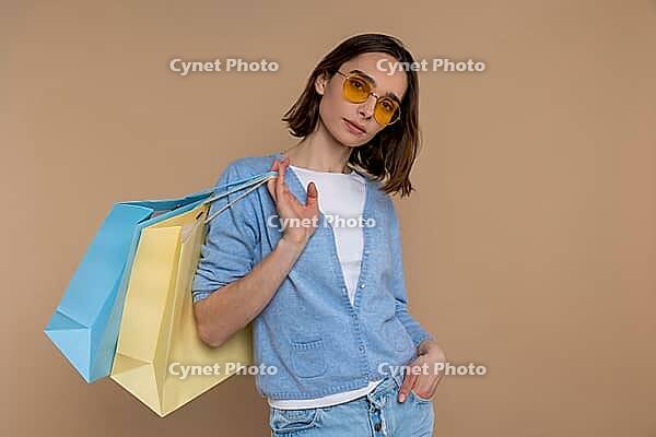 Confident fashion woman in casual clothing holding shopping bags spending time in mall isolated over beige background [IBR123569295]