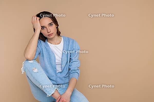 Tired woman in casual clothing leaning head on hand copy space for promotion isolated over beige background [IBR123569300]