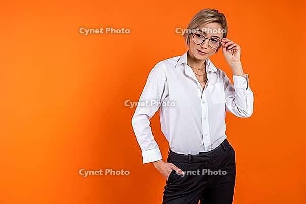 Serious woman wearing white official style shirt holding glasses looking away free space isolated over orange background [IBR123569304]