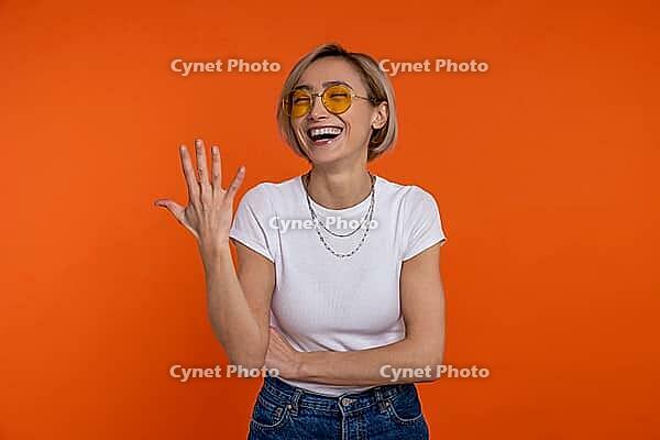 Laughing woman in white t shirt and jeans showing five fingers number isolated over orange background [IBR123569309]