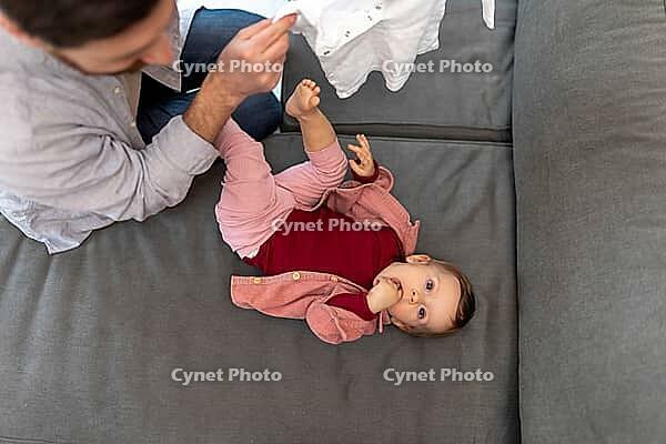 Father with toddler daughter at home, taking care of his baby changing clothes [IBR123569315]