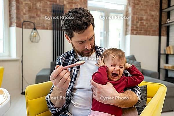 Little child care. Father feeding crying capricious infant daughter sitting at home in modern interior [IBR123569316]