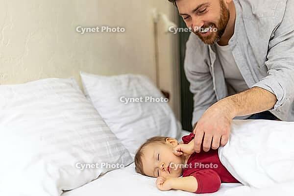 Father looking at his sleeping baby tenderly in home bedroom interior [IBR123569332]