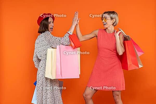 Happy women friends with shopping bags giving high five isolated over orange background [IBR123569340]