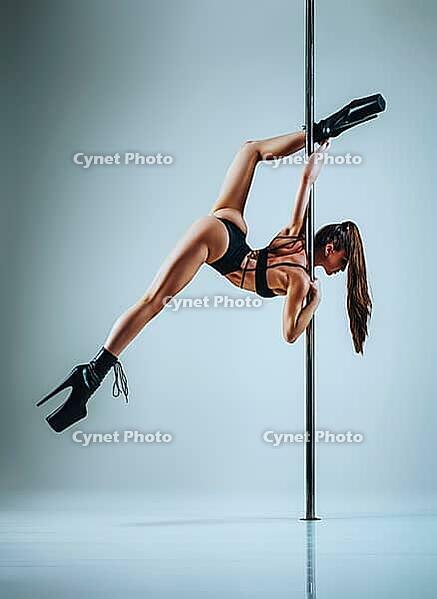 Young slim sexy brunette woman in lingerie pole dancing on white wall background [IBR123569348]