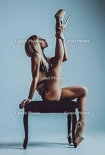 Young slim woman in lingerie sitting on stool and stretching up leg [IBR123569354]
