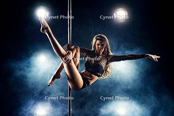 Young slim sexy woman pole dancing in club interior with lights and smoke [IBR123569356]
