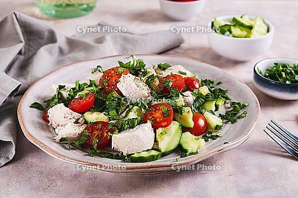 Homemade salad with cucumber, tomatoes, chicken and herbs on a plate on the table [IBR123629683]