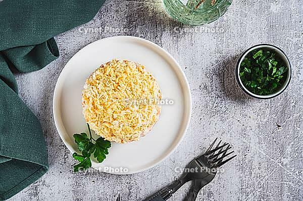 Traditional layered salad with canned fish on a plate on the table top view [IBR123629684]