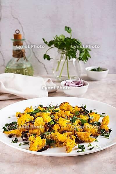 Baked small cauliflower steaks with onions and herbs on a plate on the table vertical view [IBR123629692]