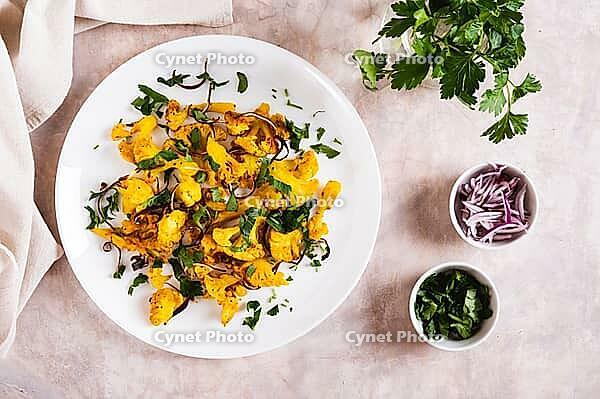 Baked small cauliflower steaks with onions and herbs on a plate on the table top view [IBR123629695]