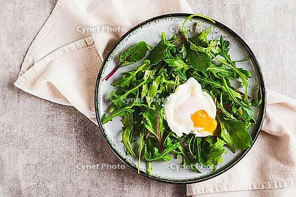 Close up of poached egg in arugula and chard leaves on a plate on a table top view [IBR123629696]