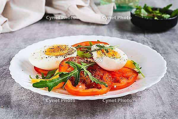 Light appetizer of tomatoes, boiled egg, cheese and arugula on a plate on the table [IBR123629699]
