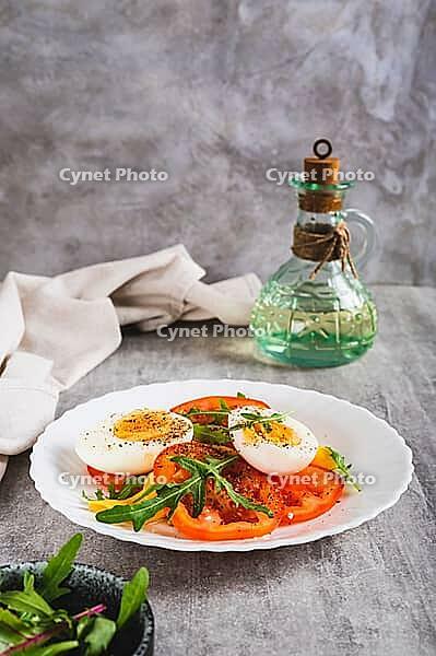 Light appetizer of tomatoes, boiled egg, cheese and arugula on a plate vertical view [IBR123629704]