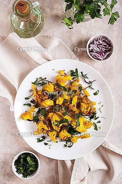 Baked spicy cauliflower with onions and parsley on a plate on the table top and vertical view [IBR123629706]