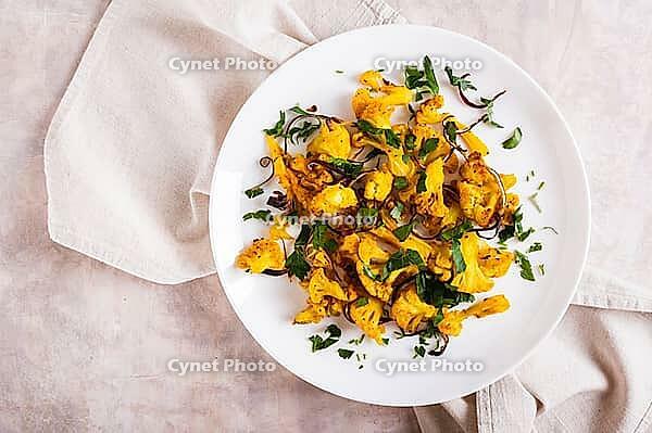 Close up of baked small cauliflower steaks with onions and herbs on a plate on the table top view [IBR123629709]