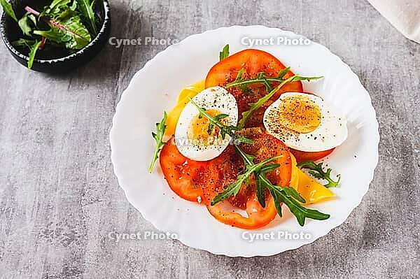 Tomato slices, egg, cheese and herbs on a plate on the table [IBR123629716]