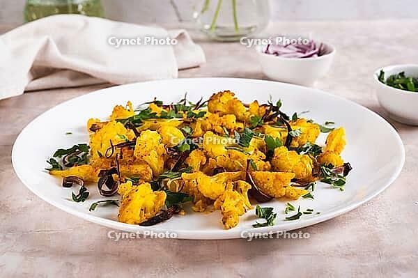 Baked small cauliflower steaks with onions and herbs on a plate on the table [IBR123629718]