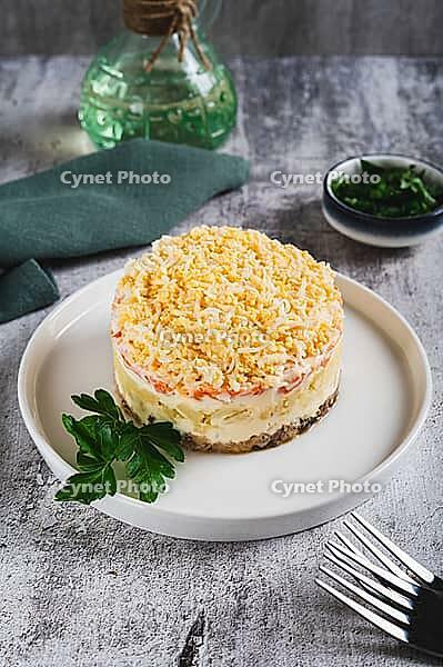 Classic mimosa salad with canned fish and vegetables on a plate on the table vertical view [IBR123629719]