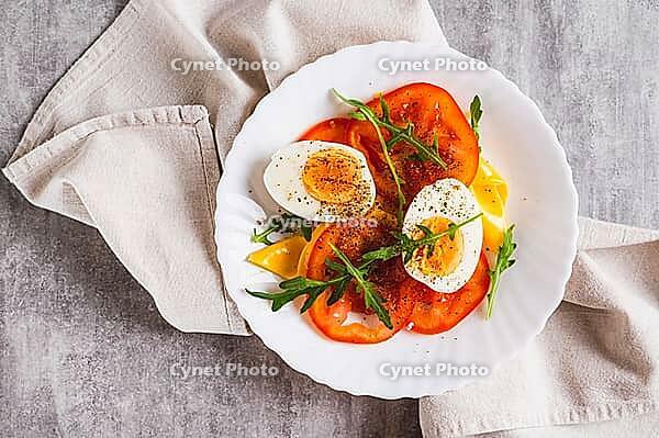 Close up of light appetizer of tomatoes, boiled egg, cheese and arugula on a plate top view [IBR123629725]