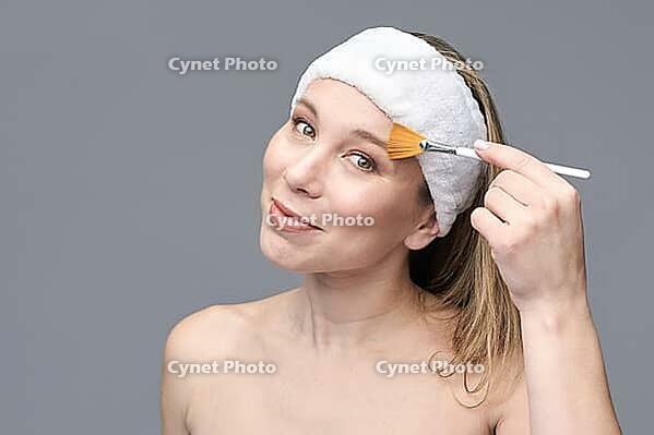 Caucasian female adult applying facial mask with brush for skincare [IBR123629738]