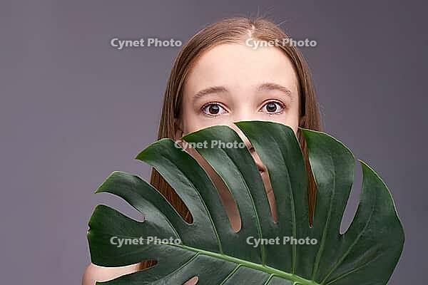 Young caucasian female with monstera leaf against gray background, expressive eyes, natural beauty [IBR123629747]