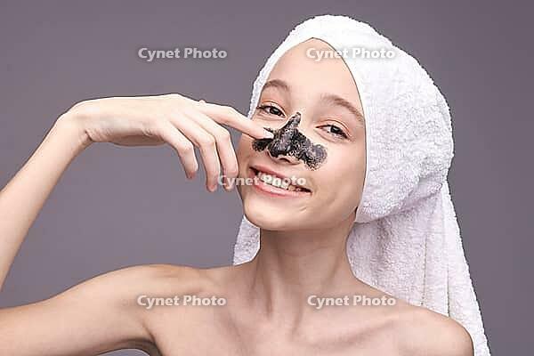 Young caucasian female skincare routine with facial mask and white towel on head smiling [IBR123629751]