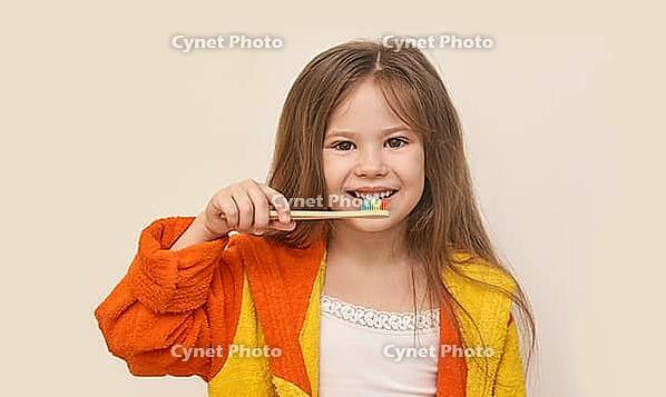 Caucasian young girl brushing teeth with colorful toothbrush in yellow orange bathrobe smiling healthy hygiene [IBR123629752]