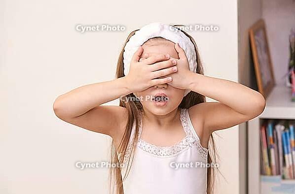Caucasian female child in white tank top covering eyes with hands in playful pose [IBR123629754]