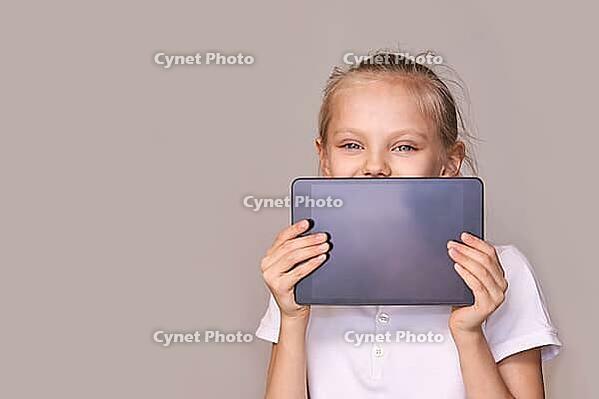 Smiling caucasian young female child holding tablet against beige background [IBR123629755]