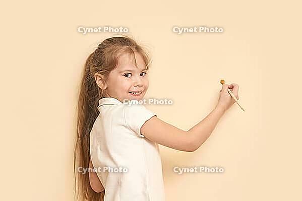 Caucasian female child painting wall with brush smiling long hair creative activity [IBR123629756]