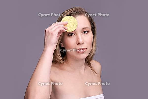 Caucasian female adult skincare routine with natural sponge on grey background [IBR123629762]