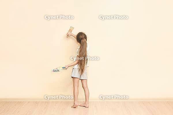Young caucasian girl painting wall with brush in minimalistic room interior [IBR123629764]