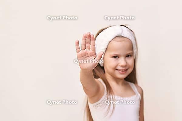 Young caucasian female child with headband making hand gesture against neutral background [IBR123629766]