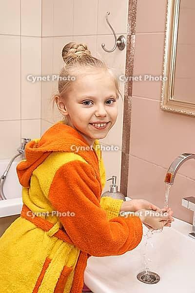 Caucasian female child in colorful bathrobe washing hands in bathroom smiling [IBR123629768]