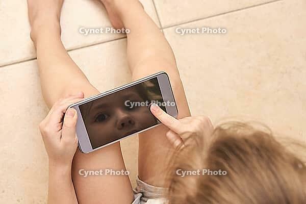 Young caucasian child engaged with smartphone technology reflection on screen [IBR123629769]
