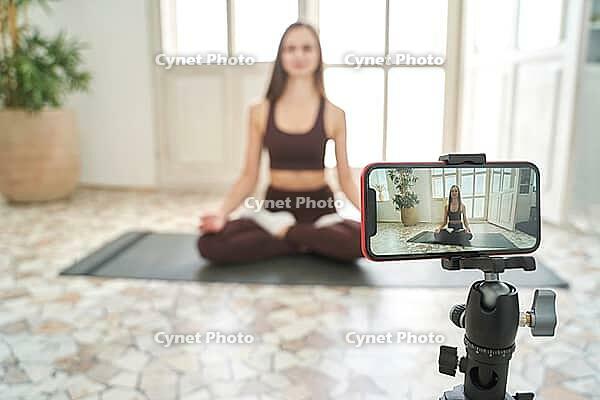 Young woman going yoga exercise at home. Health care online lessons. Indoor fitness workout. Remote sport trainer. Morning activity. Floor pilates mat. Female person lifestyle. Asana pose [IBR123638350]