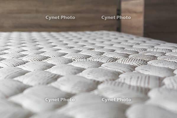 Close-up of white textured mattress surface with soft quilted pattern, in cozy bedroom interior with wooden furniture, concept of comfort, sleep and relaxation [IBR123638374]