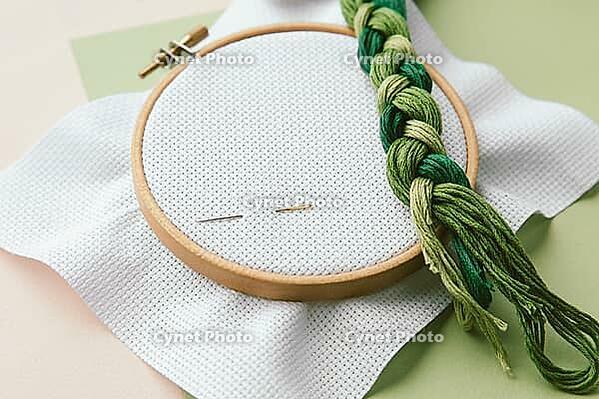 Embroidery tools wooden hoop, green embroidery floss, and needles on white fabric, arranged for needlework and crafting, cross stitch concept [IBR123638384]